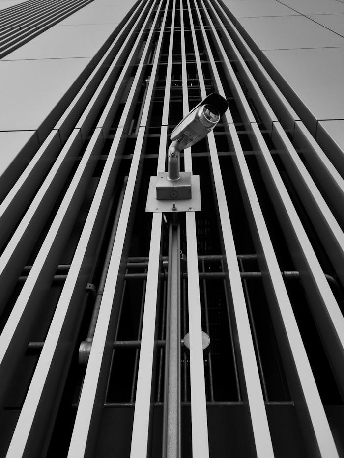 Black and white close-up of a surveillance camera on a modern building facade.